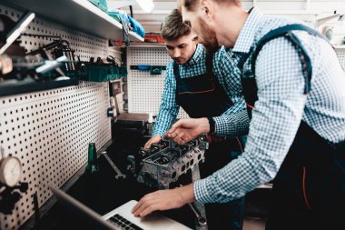 İki otomatik mekanik birlikte garajda çalışır. Kullanarak anahtarı. Dizüstü ekran bakıyor. Bilgi paylaşımı. Profesyonel üniforma. Kendine güvenen mühendislik uzman ekip. Servis istasyonu kavramı.