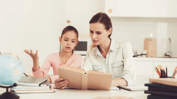 Mom Helps Daughter To Do Homework In The Kitchen. Family Relationship Concept. Educational Childhood. Studying At Home. Knowledge Receiving. Information Writing. Parents Duty. Working Together.