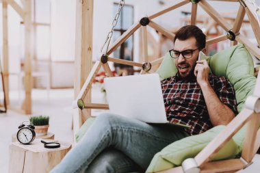 Fikirler oluşturur. Smartphone. Sandalyeye asılı. Dizüstü bilgisayar. Otur. Beyin fırtınası. Genç bir adam. İş adamı. Ofiste çalışıyor. Yaratıcı işçi. İş adamları. Çalışma alanı. İlham. Gevşeme. Rahat Office.