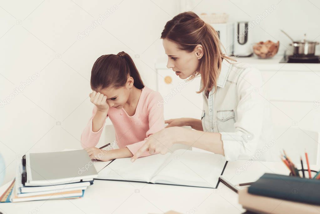 Mom Helps Daughter To Do Homework In The Kitchen. Family Relationship Concept. Educational Childhood. Studying At Home. Knowledge Receiving. Information Writing. Parents Duty. Working Together.