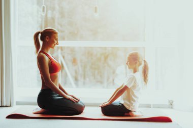 Anne ve kızı spor salonu halı üzerinde oturuyor. Yoga kavramı. Meditasyon poz. Aktif yaşam tarzı. Birbirlerine bakıyorlar. Evde Fitness. Holiday Leisure. Vücut dengesi. Spor egzersiz. Güneşli sabah.