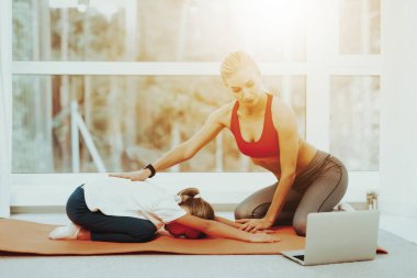 Anne ve kızı geri germe. Dizüstü ekran. Aktif yaşam tarzı. Birlikte rahatlatıcı. Evde Fitness yapıyor. Holiday Leisure. Vücut dengesi. Spor egzersiz. Spor salonu halı üzerinde döşeme. Yoga eğitim.