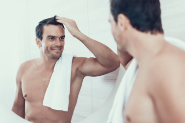 Mutlu adam banyoda ayna yansıması görünüyor. Yakışıklı gülümseyen neşeli beyaz kahverengi saçlı Genç insanla omuz kol ayak uydurarak havlu ile çıplak göğüs portresi