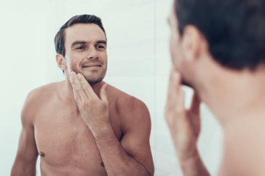 Banyo onay sakal tıraş sonra mutlu adam. Neşeli beyaz kahverengi saçlı genç kişi ile gülümseyen portresi göğüs çıplak ve ayna bakarak ve yansıma keyfini çıkarın.