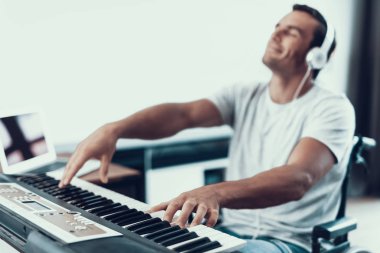 Disabled Man Playing Electric Piano in Headphones. Portrait of Handsome Young Handicapped Man in Wheelchair Playing Music on Synthesizer with Closed Eyes While Sitting in Living Room at Home. clipart
