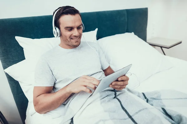 Young Man Uses Pad Listens Music Bed Guapo Alegre Sonriente —  Fotos de Stock