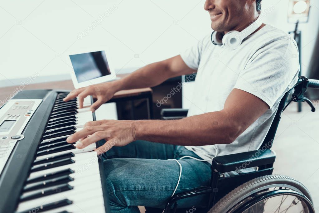 Closeup of Disabled Male Hands Plays Synthesizer. Happy Young Handicapped Man in Wheelchair Wearing White T-Shirt and Blue Jeans Playing Music on Synthesizer While Sitting in Living Room at Home