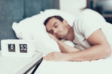 Alarm beyaz keten ile yatakta yakınındaki kişi uyur. Yatak odasında Modern daire içinde yatan yakışıklı delikanlı. Eller başının altına tutmak ve beyaz T-shirt giyen kapalı gözler olan adam. Sabah kavramı