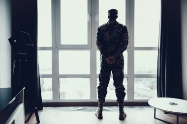 Arkadan görünüşü pencere yakınındaki askeri üniformalı erkeklere. Arkasından geçtim ve geniş panoramik pencere askerlik kavramı seyir silah ile Modern daire içinde duran ciddi düşünceli kişi