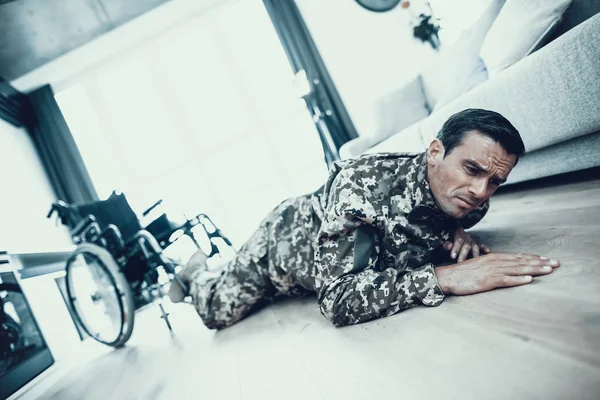 Disabled Man in Uniform Fell from Wheelchair. Handsome Caucasian Handicapped Person Lying on Floor and Try to Get Up. Invalid Chair Parked Behind Man in Bright Modern Living Room