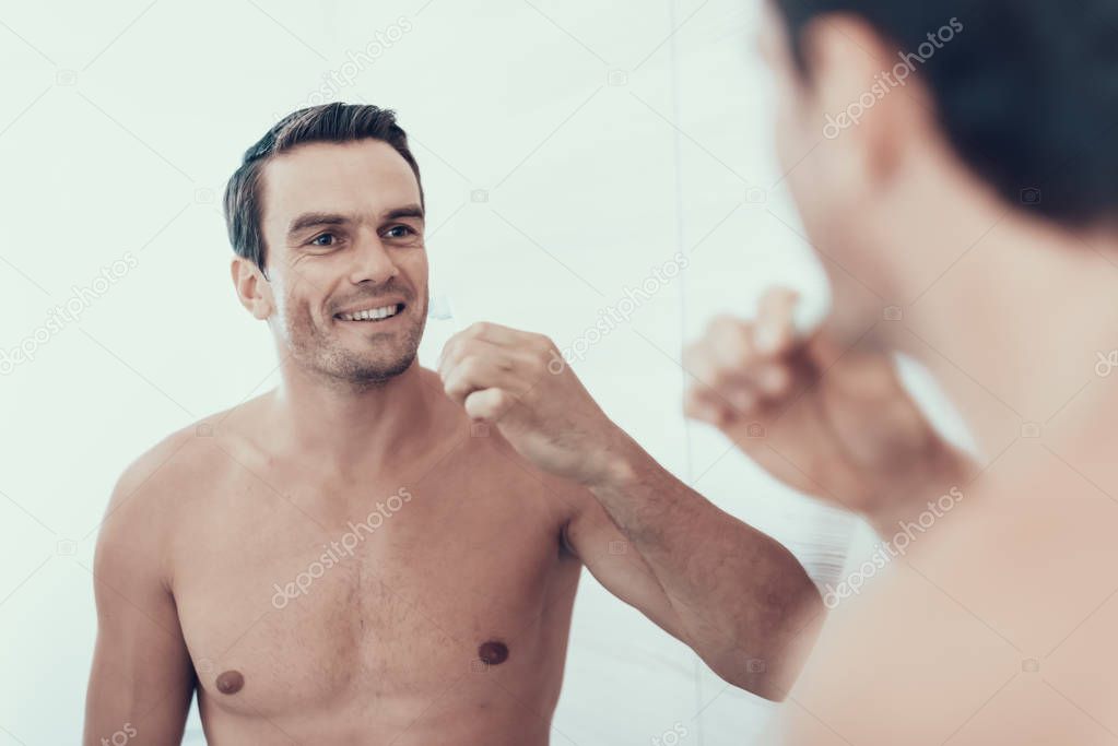 Mirror Reflection of Man Brush Teeth in Bathroom. Portrait of Smiling Handsome Brown Haired Young Person with Bare Chest Holding Toothbrush and Looking at Mirror. Morning Concept