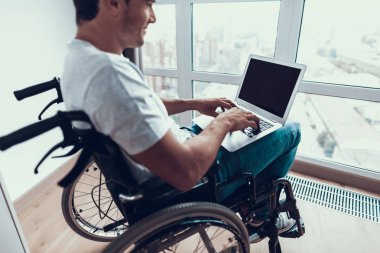 Engelli adam Holding Laptop ve kucağına yazarak. Portre yakışıklı kişinin T-Shirt giyiyor ve tekerlekli sandalye Gözatma sayısı Internet ve iç ağ kot oturur. Sakatlık ve iş kavramı