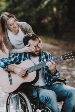 Engelli adam parkta gitar çalmak tekerlekli sandalye üzerinde. Engelli genç adam genç mutlu bir kadın. Yaz Park'ta rahatlatıcı. Eğlenceli yaz Park. Kurtarma ve sağlık kavramları. Neşeli insanlar.