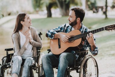 Engelli adam parkta gitar çalmak tekerlekli sandalye üzerinde. Genç adam kadın tekerlekli sandalye üzerinde devre dışı. Yaz Park'ta rahatlatıcı. Eğlenceli yaz Park. Kurtarma ve sağlık kavramları. Neşeli insanlar.