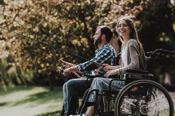 在公园里有钓鱼竿的轮椅人 轮椅上残疾的年轻男子妇女 在夏季公园放松身心 夏季公园野餐 恢复和医疗保健概念 开朗的人 — 图库照片