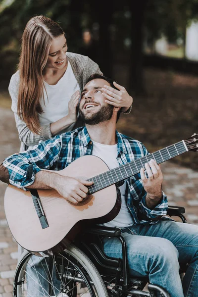 Engelli adam parkta gitar çalmak tekerlekli sandalye üzerinde. Genç adam kadın tekerlekli sandalye üzerinde devre dışı. Yaz Park'ta rahatlatıcı. Eğlenceli yaz Park. Kurtarma ve sağlık kavramları. Neşeli insanlar.