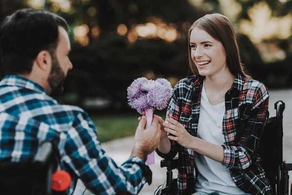 Couple of Disabled People on Wheelchairs on Date in Park. Young Man with Flowers. Woman on Wheelchair. Date in Summer Park. Romantic Relationship. Recovery and Healthcare Concepts. Happy Couple.