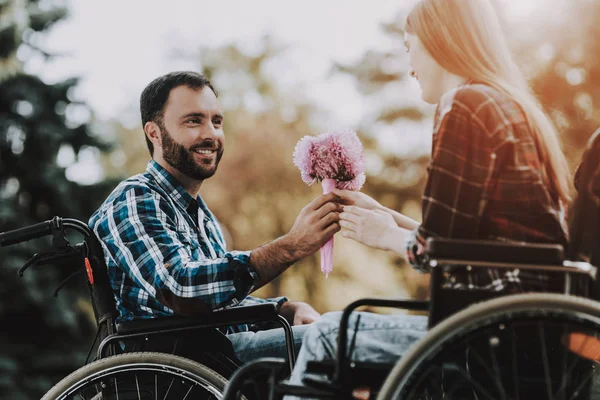 在公园约会的轮椅上有几个残疾人 有花的年轻人 轮椅上的女人在夏季公园的日期 浪漫的关系 恢复和医疗保健概念 快乐夫妇 — 图库照片