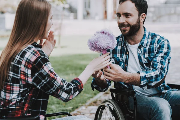 Couple of Disabled People on Wheelchairs on Date in Park. Young Man with Flowers. Woman on Wheelchair. Date in Summer Park. Romantic Relationship. Recovery and Healthcare Concepts. Happy Couple.