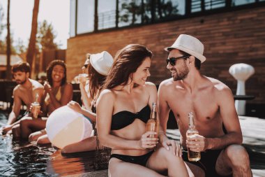 Gülümseyen iki havuz, alkollü içecekler. Güzel genç bira şişe tutan ve having Fun havuz kenarında çift. Mutlu arkadaş Enoying havuz partisi. Yaz tatili kavramı