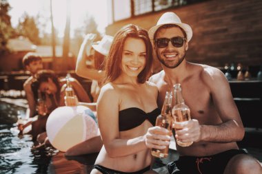 Gülümseyen iki havuz, alkollü içecekler. Güzel genç bira şişe tutan ve having Fun havuz kenarında çift. Mutlu arkadaş Enoying havuz partisi. Yaz tatili kavramı