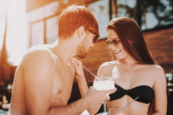 微笑的情侣在池畔喝鸡尾酒 美丽的年轻夫妇拿着眼镜与酒精饮料和有乐趣在池畔 快乐的朋友伊光能泳池派对 暑假概念 — 图库照片