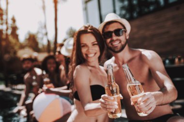Gülümseyen iki havuz, alkollü içecekler. Güzel genç bira şişe tutan ve having Fun havuz kenarında çift. Mutlu arkadaş Enoying havuz partisi. Yaz tatili kavramı
