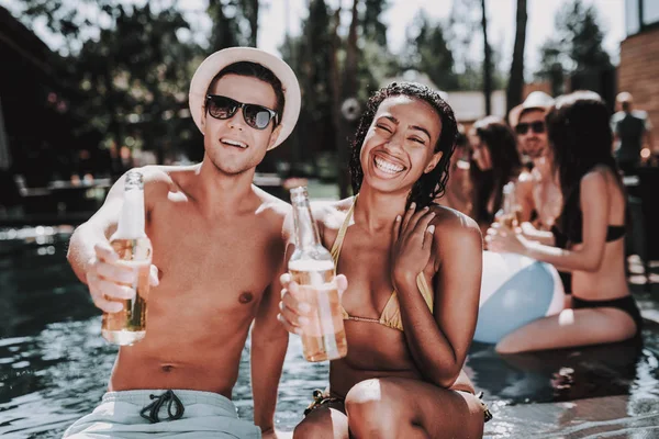 在池畔的微笑夫妇与酒精饮料 美丽的黑人妇女和年轻男子拿着瓶啤酒和乐趣在池畔 快乐的朋友 Enoying 泳池派对 暑假概念 — 图库照片