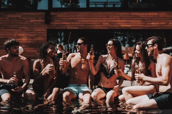在池畔喝酒的年轻朋友 一群年轻的微笑的人拿着瓶子的啤酒和乐趣在池畔 快乐的朋友 Enoying 泳池派对 暑假概念 — 图库照片