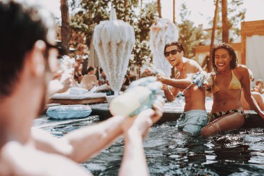 Grup arkadaşıyla genç gülümseyen havuzda eğleniyor. Genç mutlu insanlar iskambil birlikte renkli su silahlar içinde Açık Yüzme Havuzu. Arkadaşlar havuz partisinde. Yaz tatili kavramı