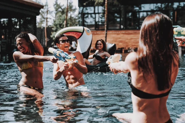 一群年轻微笑的朋友在游泳池里玩得很开心 年轻快乐的人一起玩五颜六色的水枪在室外游泳池 朋友在泳池派对 暑假概念 — 图库照片