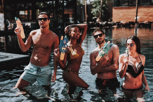 年轻的微笑的人在游泳池与水枪 年轻的快乐朋友站在一起 五颜六色的水枪在室外游泳池 泳池派对上的朋友暑假概念 — 图库照片