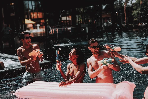 一群年轻微笑的朋友在游泳池里玩得很开心 年轻快乐的人一起玩五颜六色的水枪在室外游泳池 朋友在泳池派对 暑假概念 — 图库照片