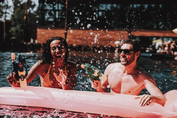 年轻的微笑的夫妇有乐趣在游泳池 年轻快乐的人一起玩五颜六色的水枪在室外游泳池 朋友在泳池派对 暑假概念 — 图库照片