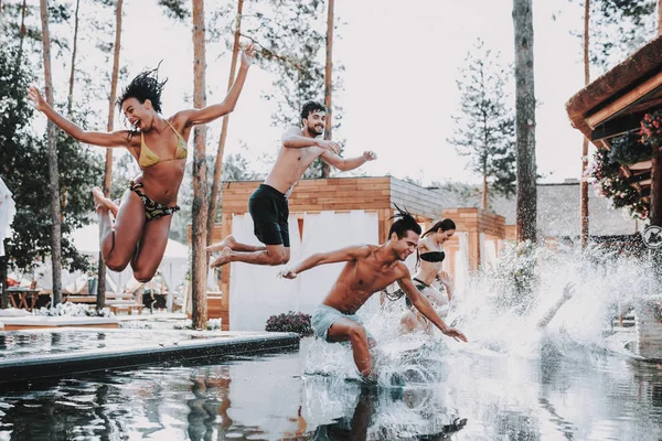 Young Smiling Friends Jumping into Swimming Pool. Group of Young Happy People having Fun by Jumping from Poolside into Water. Friends Enjoying Outdoor Pool Party. Summer Vacation Concept