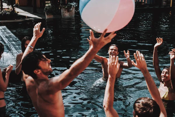 Group of Young Smiling Friends having Fun in Pool. Young Happy People Playing Together with Colorful beach Ball in Outdoor Swimming Pool. Friends at Pool Party. Summer Vacation Concept