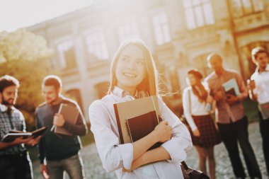 Üniversitede ayakta. Kız. Mutlu. Öğrenciler. Avlu. Kitaplar. İyi bir ruh hali. Üniversitesi. Bilgi. Mimarisi. Mutluluk. İstihbarat. Diploma. Kutlama. Kampüs. Erkek arkadaş.