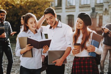 Güneşli bir gün. Öğrenciler. İki kız ve erkek. Birlikte. Avlu. Kitap tutan. Üniversitede ayakta. İyi bir ruh hali. İstihbarat. Birlikte ayakta. Dışarıda. Arkadaşlar. Mutlu. Kitaplar. Üniversitesi. Bilgi.