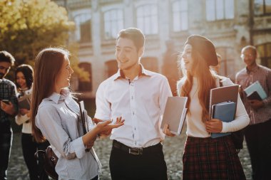 İki kız ve erkek. Birlikte. Avlu. Güneşli bir gün. Öğrenciler. Kitap tutan. Üniversitede ayakta. İyi bir ruh hali. İstihbarat. Birlikte ayakta. Dışarıda. Arkadaşlar. Mutlu. Kitaplar. Üniversitesi. Bilgi.