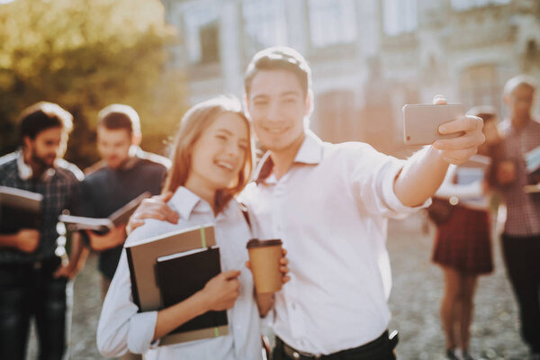 Holding Books. Standing in University. Good Mood. Intelligence. Man and Woman. Standing Together. Outside. Sunny Day. Students. Friends. Happy. Courtyard. Books. University. Knowledge.