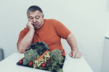 Vejetaryen yiyecekler ile tepsi ile şişman üzgün adam. Bulimia olan adam. Sağlıksız yaşam tarzı kavramı. Adam üzgün adam kilolu tedavisinde oturuyor. Kilolu olan adam. Sağlıklı ve vejetaryen gıda.