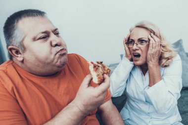 Doktor şişman adam pizzayla yakınındaki paltolu üzgün. Bulimia olan adam. Sağlıksız yaşam tarzı kavramı. Pizza yemek adam oturuyor. Beyaz önlük kadında. Hasta mide ile. Kilolu adamla.