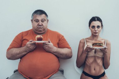Şişman adam ve gıda ile plakalı anoreksik kız. Anoreksiya kadınla. Kız beyaz plakalı. Diyet ve sağlık kavramı. Bulimia olan adam. Sağlıksız yaşam tarzı kavramı. Kilolu adamla.
