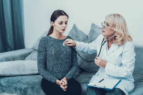 年轻的苗条的女人在灰色毛衣访问医生 穿白衣的女人饮食和保健概念 用听诊器做的多镜 灰色沙发上的女人 医疗设备 眼镜中的妇女 — 图库照片