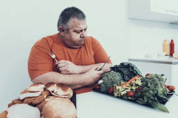 Üzgün şişko tepsileri ile beyaz masasına yemek ile. Bulimia olan adam. Sağlıksız yaşam tarzı kavramı. Oturan adam üzgün adam tepsi hamburger ile. Kilolu olan adam. Sağlıklı ve vejetaryen gıda.