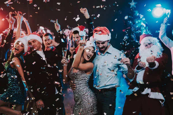 Happy Young People Dancing on New Year Party. Santa Claus. People in Red Caps. Happy New Year Concept. Glass of Champagne. Celebrating of New Year. Young Woman in Dress. Men in Suits.