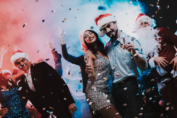 Happy Young People Dancing on New Year Party. Santa Claus. People in Red Caps. Happy New Year Concept. Glass of Champagne. Celebrating of New Year. Young Woman in Dress. Men in Suits.