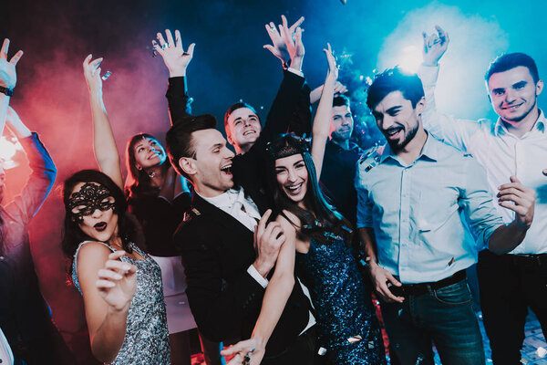 Smiling People Celebrating New Year on Party. Happy New Year. People Have Fun. Indoor Party. Celebrating of New Year. Young Woman in Dress. Young Man in Suit. Exited People. Hands Up.