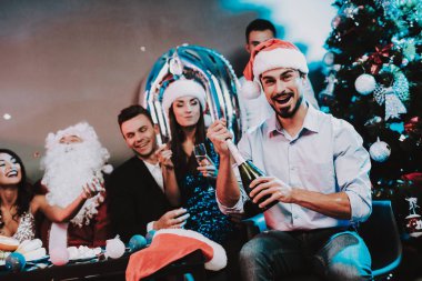 Rad Cap açılış şişe şampanya erkekte sakallı. Santa Claus Costume. İnsanlar kırmızı kapaklar. Mutlu yeni yıl kavramı. Şişe şampanya. Yeni yıl kutlama. Elbiseli Genç kadın.