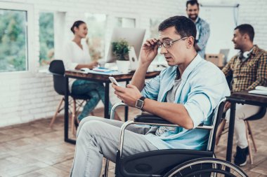Tekerlekli sandalye ile telefon ofiste gözlüklü adam. Evet. Genç adam adam tekerlekli sandalye üzerinde devre dışı. Kurtarma ve sağlık kavramları. Office çalışmasında. Genç bir işçi. Oturan adam.